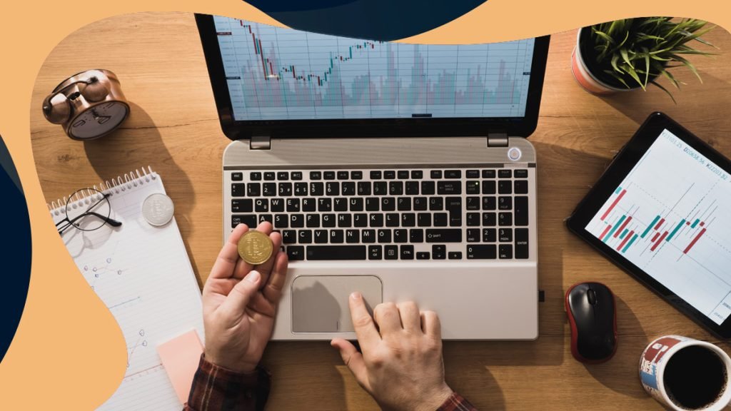 Hombre mirando un gráfico de criptodivisas en un ordenador portátil y sosteniendo una moneda Bitcoin física. 